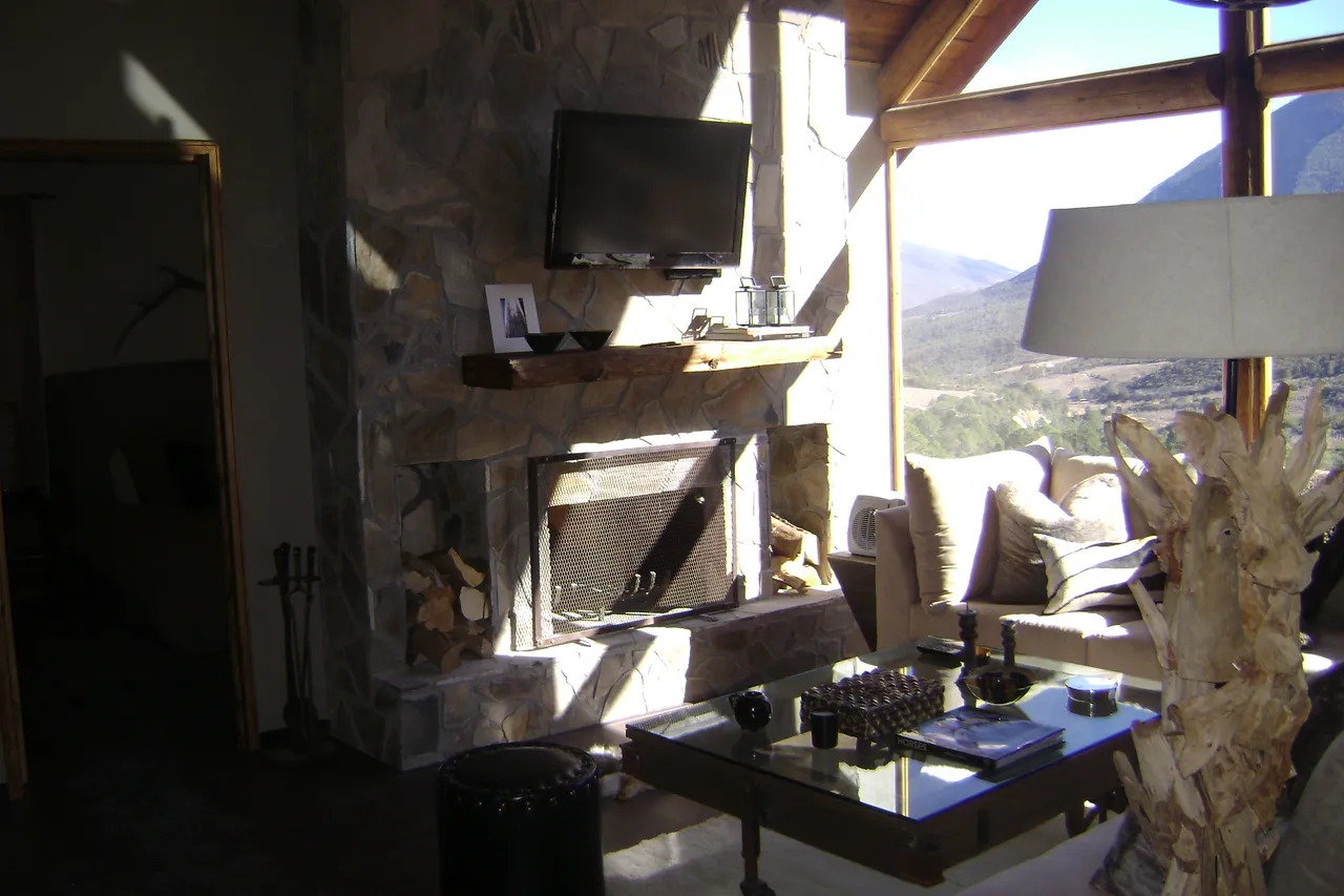 Interior terminado con chimenea de piedra laja, duela laminada y ventanal a la sierra